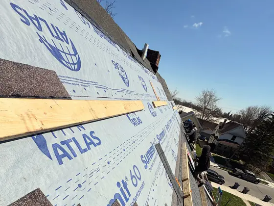 Synthetic underlayment and the first shingle courses running up a roof, nail gun in the foreground.