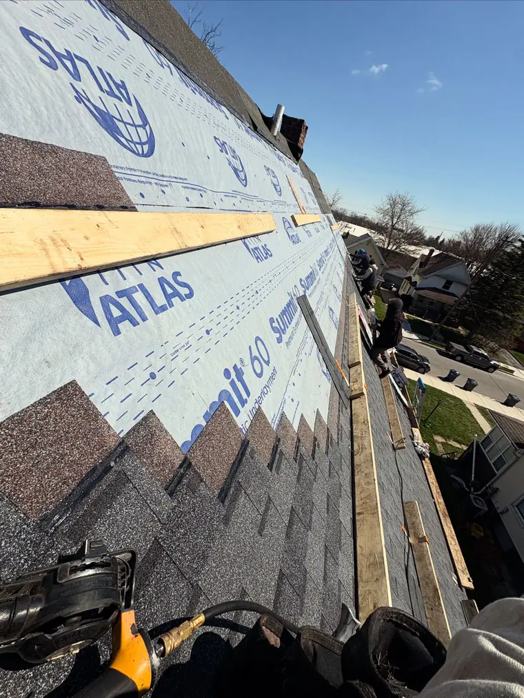 Synthetic underlayment and the first shingle courses running up a roof, nail gun in the foreground.