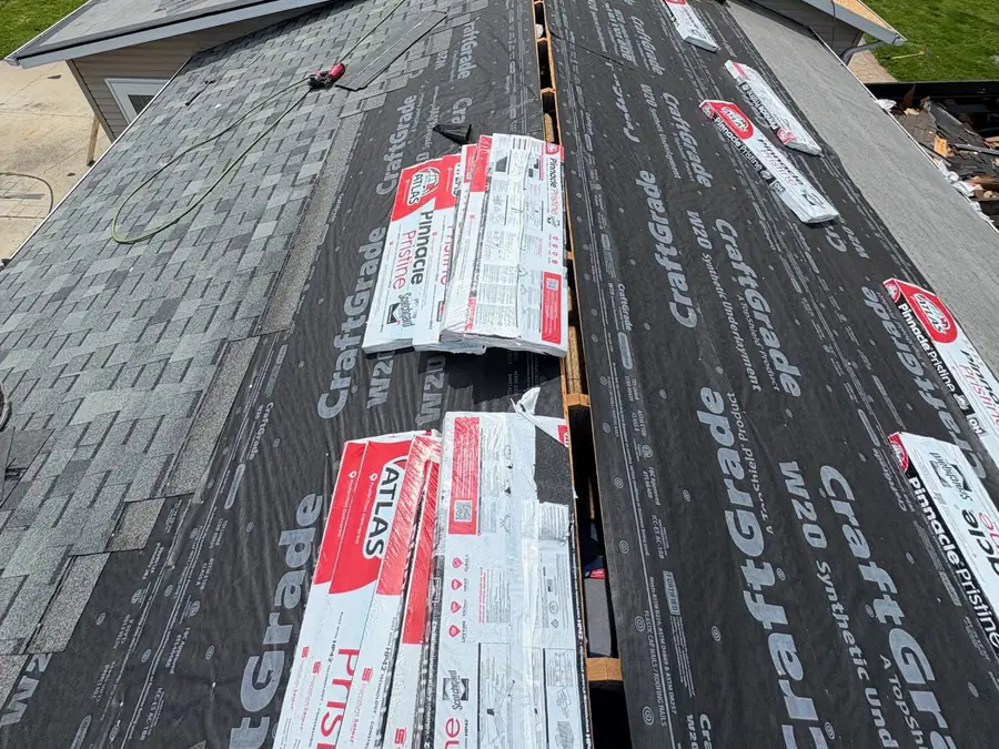 Shingle bundles staged along a stripped roof with the crew working at the ridge.