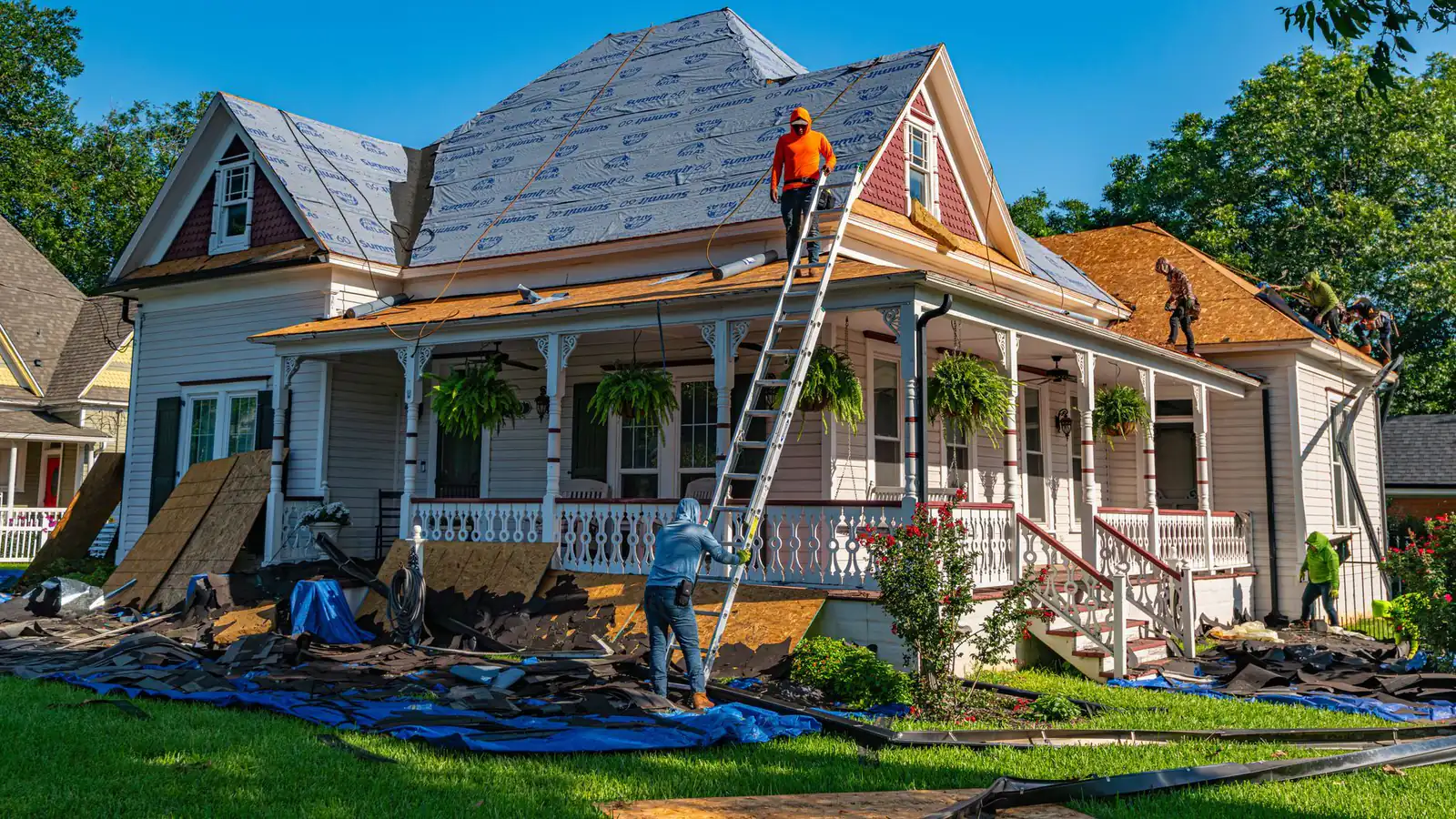 Roofers working on a house with a ladder up to a partly re-shingled roof.