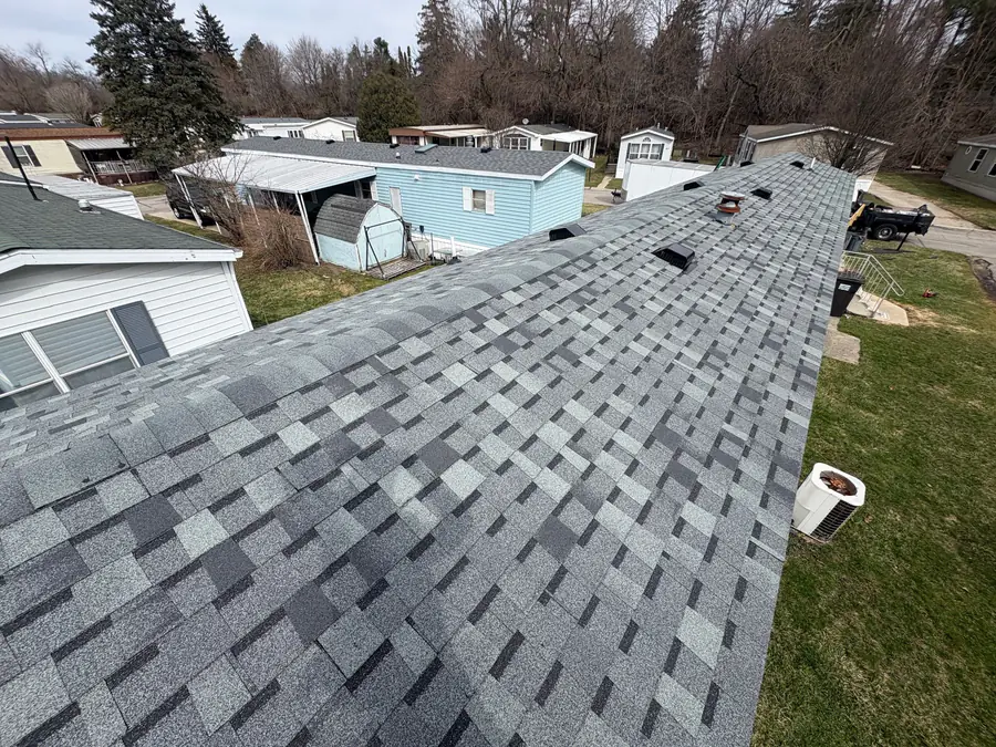 A finished grey shingle roof ridge with a Michigan neighbourhood behind it.