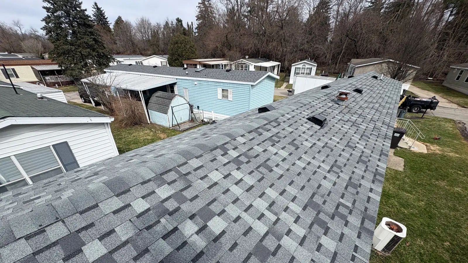 A finished grey shingle roof ridge with a Michigan neighbourhood behind it.