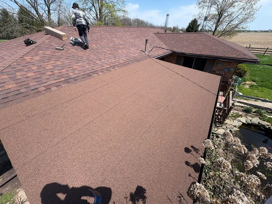 A Joe’s Roofing crew member walking a red-brown shingle roof on a ranch house.