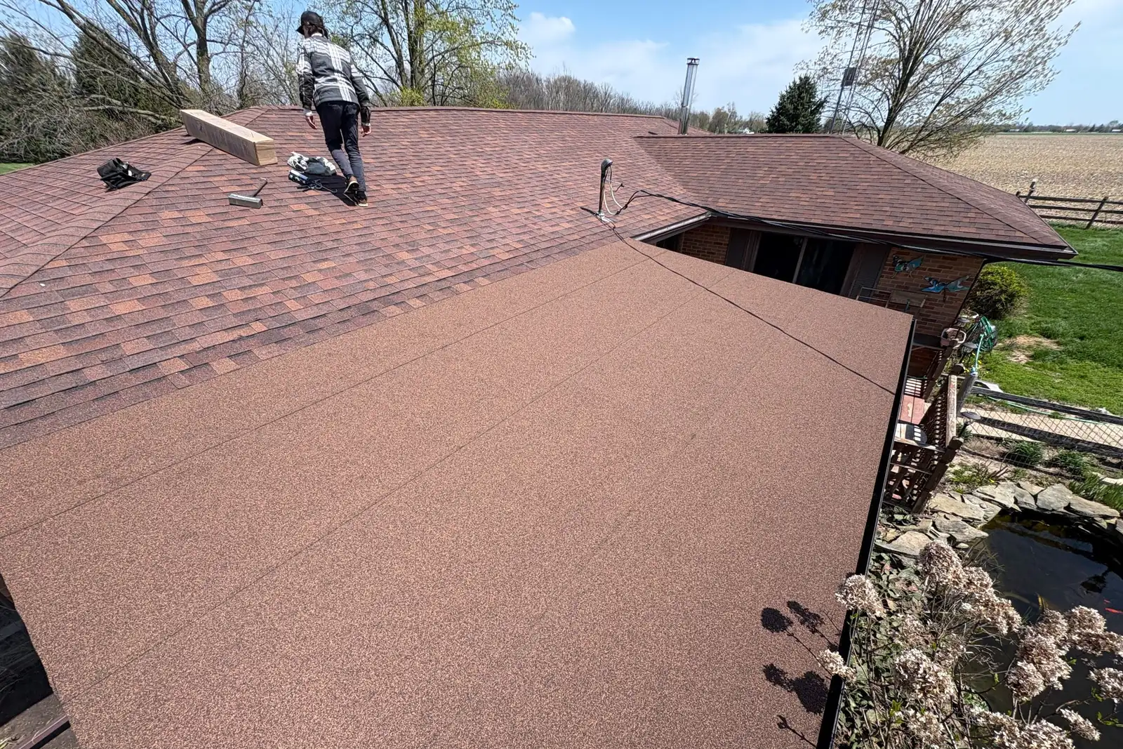 A Joe’s Roofing crew member walking a red-brown shingle roof on a ranch house.
