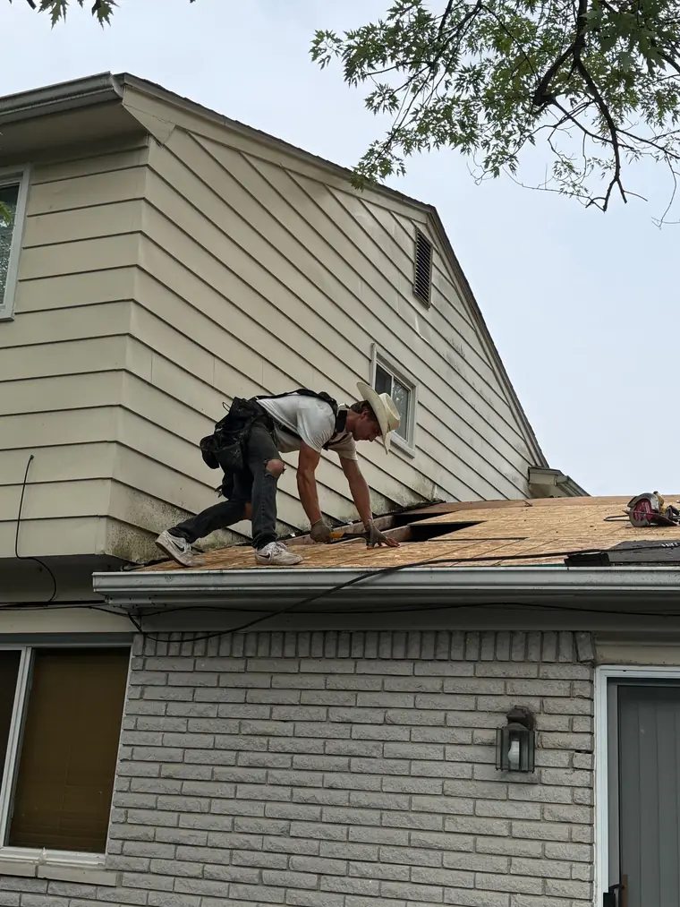 A roofer tearing off old shingles down to the deck on the gable end of a two-storey house.