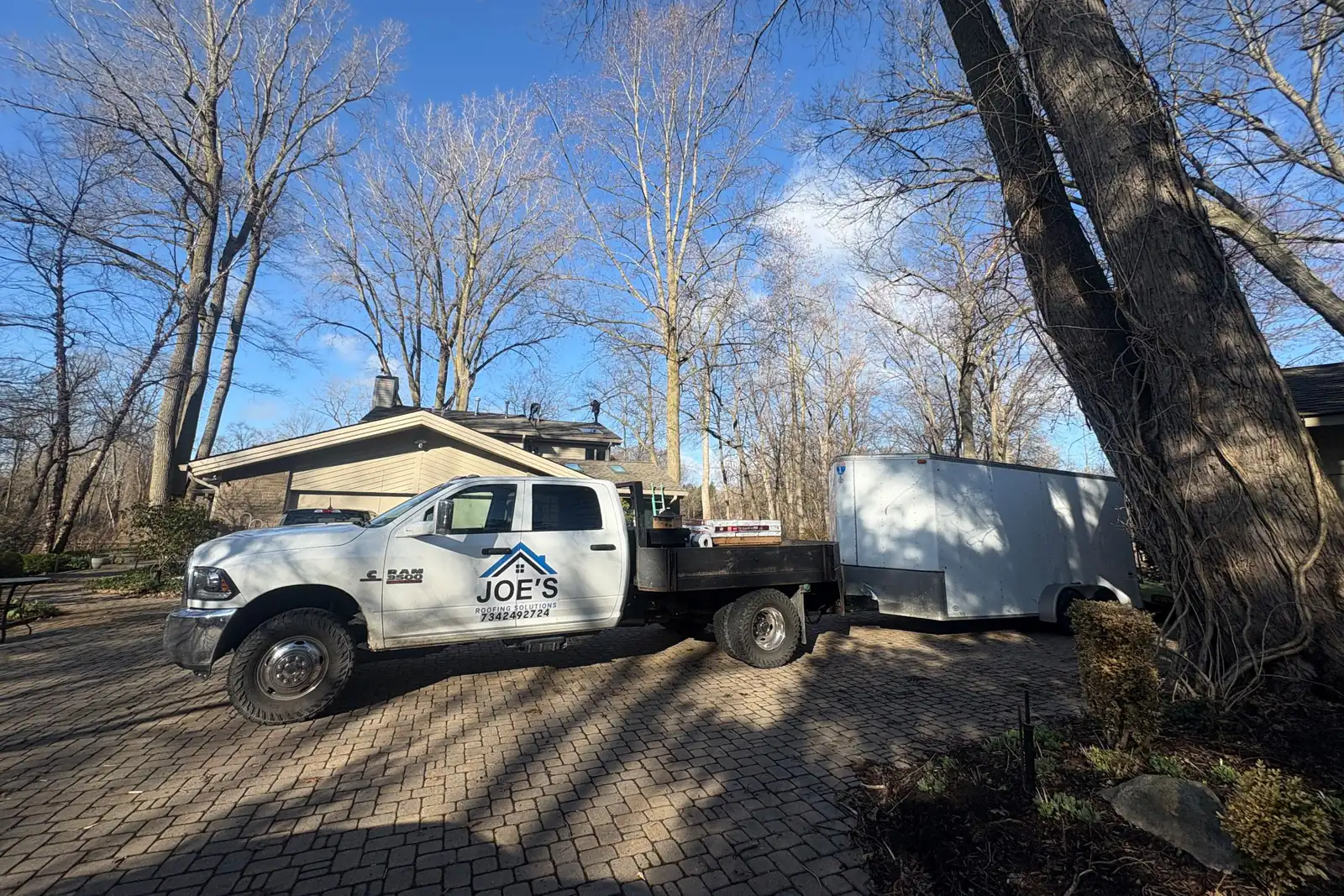 The Joe’s Roofing Solutions flatbed truck and enclosed trailer parked in a customer’s driveway.