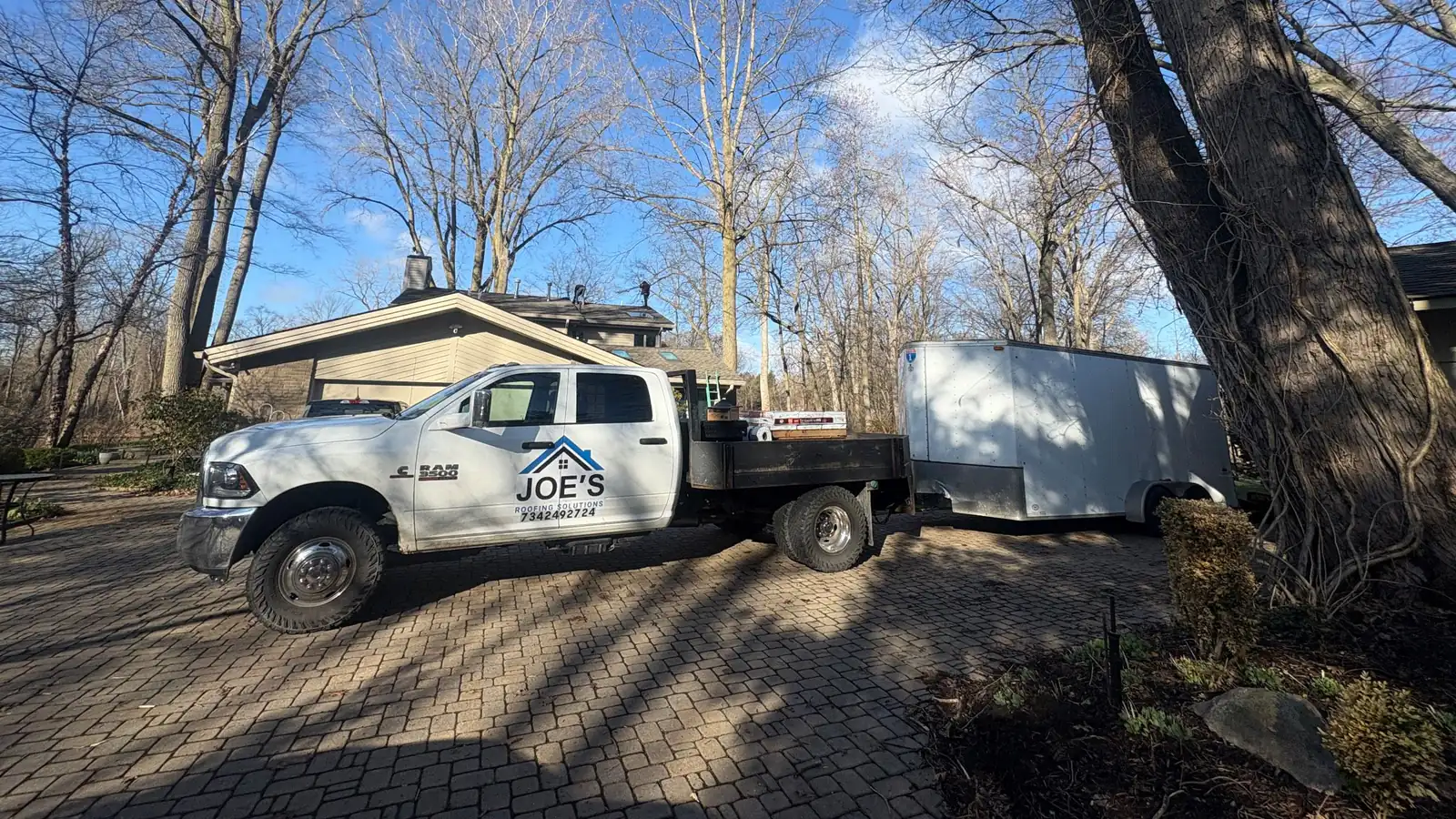 The Joe’s Roofing Solutions flatbed truck and enclosed trailer parked in a customer’s driveway.